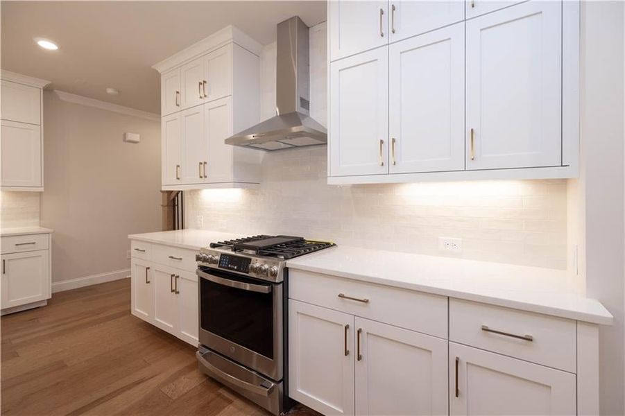 Kitchen with gas stove, white cabinetry, wall chimney range hood, crown molding, and dark wood-style flooring