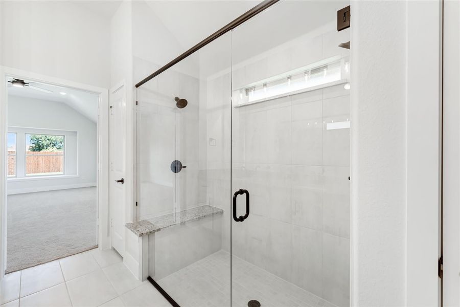 Walk-in shower with glass door, white tile walls, built-in bench, and dark bronze fixtures