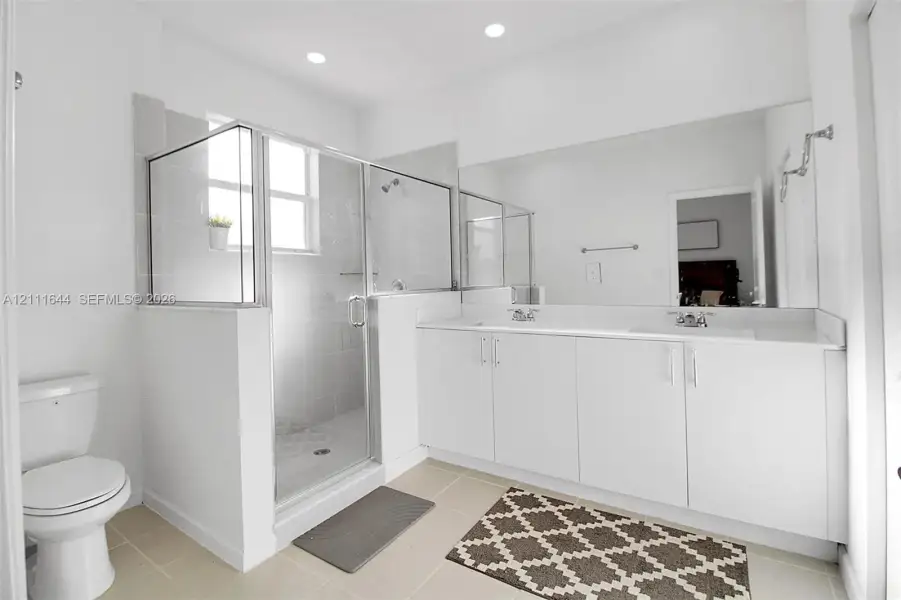 Double vanity with white cabinetry and solid surface countertop, large wall-mounted mirror, and glass-enclosed shower with tiled surround Double vanity with white cabinetry and solid surface countertop, large wall-mounted mirror, and glass-enclosed shower with tiled surround