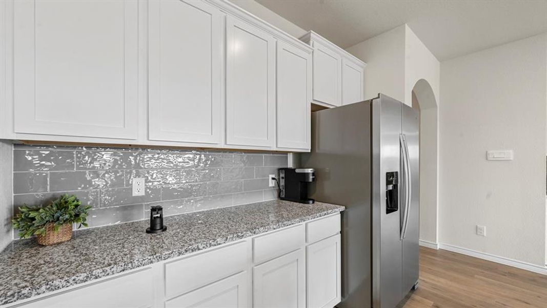 Kitchen featuring light stone countertops, light wood-style floors, stainless steel fridge with ice dispenser, arched walkways, and white cabinets