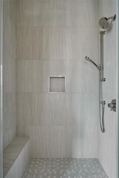 Shower featuring light-toned large format wall tile, a mosaic tile floor, a built-in bench, and a recessed niche