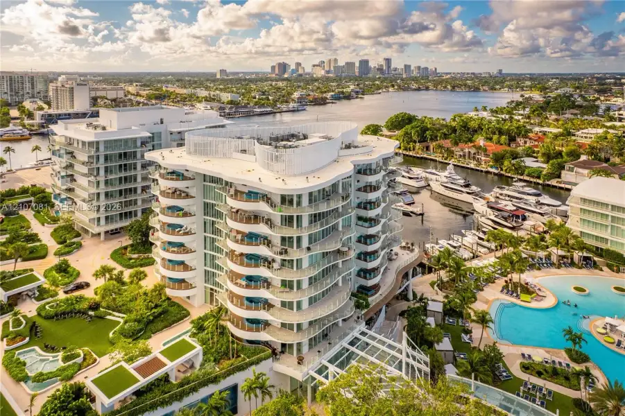 High-rise residential building featuring curved exterior balconies, glass railings, deep-water boat slips, a resort-style swimming pool, and landscaped grounds High-rise residential building featuring curved exterior balconies, glass railings, deep-water boat slips, a resort-style swimming pool, and landscaped grounds