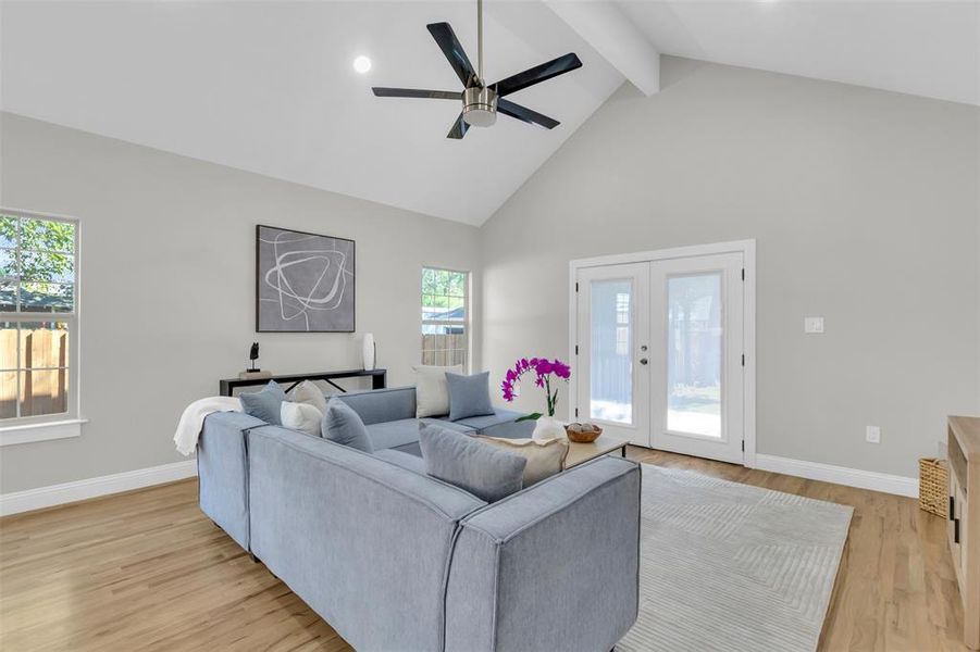 Living area with beam ceiling, high vaulted ceiling, french doors, light wood finished floors, and ceiling fan