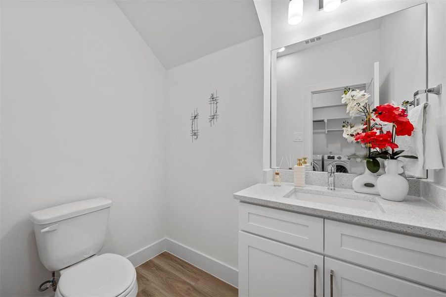 Half bathroom featuring visible vents, toilet, wood finished floors, washer and dryer, and vanity