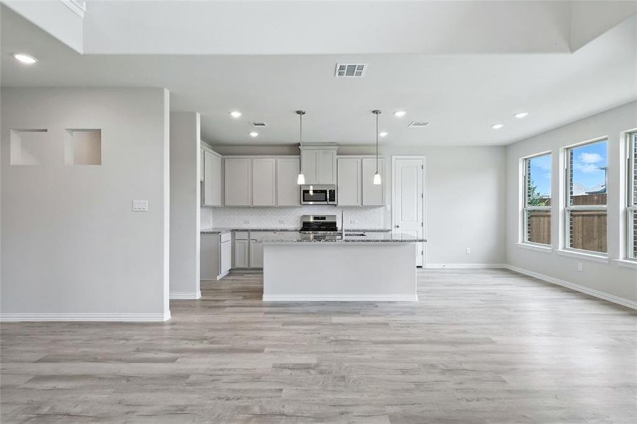 Kitchen with stainless steel microwave, light wood finished floors, open floor plan, recessed lighting, and decorative backsplash Kitchen with stainless steel microwave, light wood finished floors, open floor plan, recessed lighting, and decorative backsplash