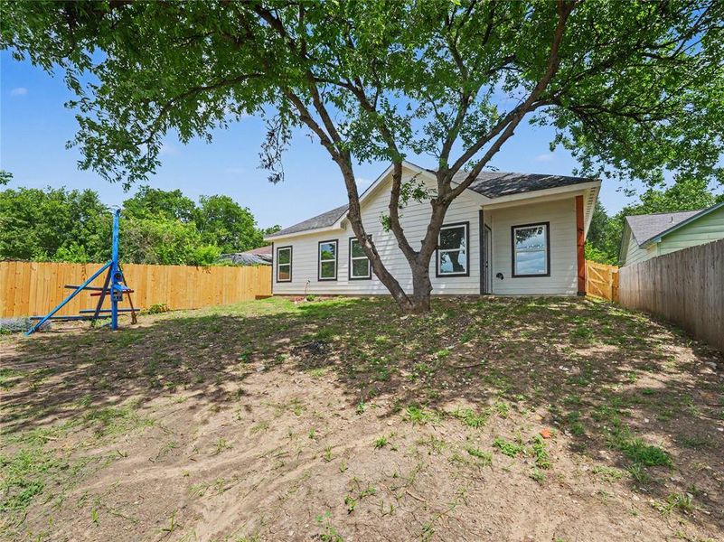 Expansive backyard featuring a mature shade tree, a newly installed wood privacy fence, and a white siding exterior with contrasting dark window frames Expansive backyard featuring a mature shade tree, a newly installed wood privacy fence, and a white siding exterior with contrasting dark window frames