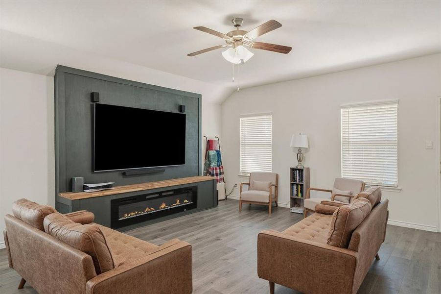 Living area with a ceiling fan, wood finished floors, a glass covered fireplace, and vaulted ceiling Living area with a ceiling fan, wood finished floors, a glass covered fireplace, and vaulted ceiling