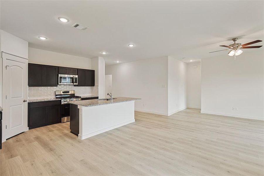 Kitchen with tasteful backsplash, a center island with sink, light stone counters, light hardwood / wood-style flooring, and stainless steel appliances