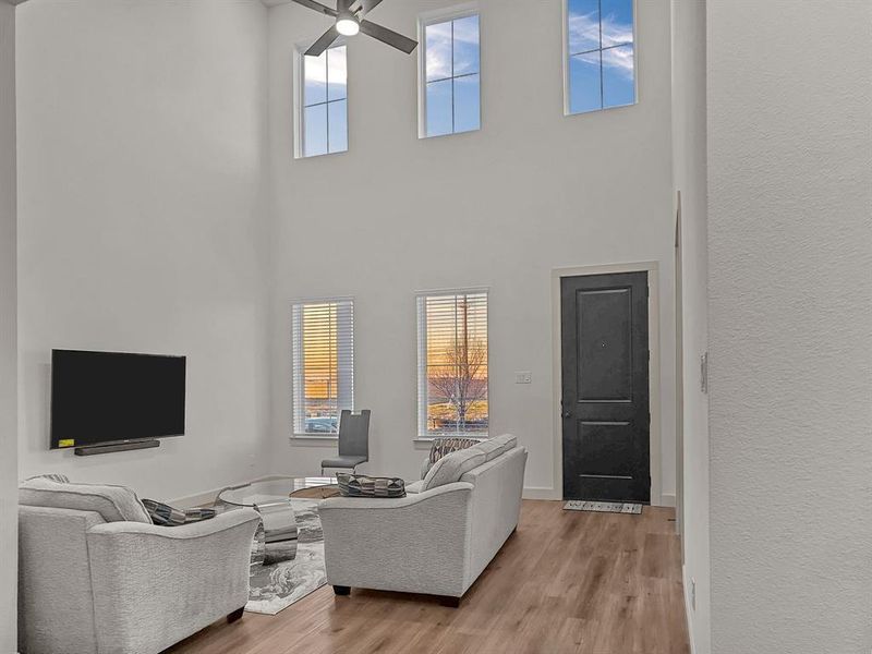 Living room with a high ceiling, ceiling fan, light hardwood / wood-style floors, and a wealth of natural light