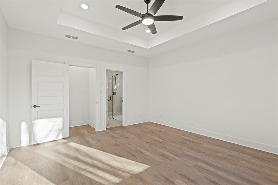 Unfurnished bedroom with baseboards, visible vents, a raised ceiling, and wood finished floors