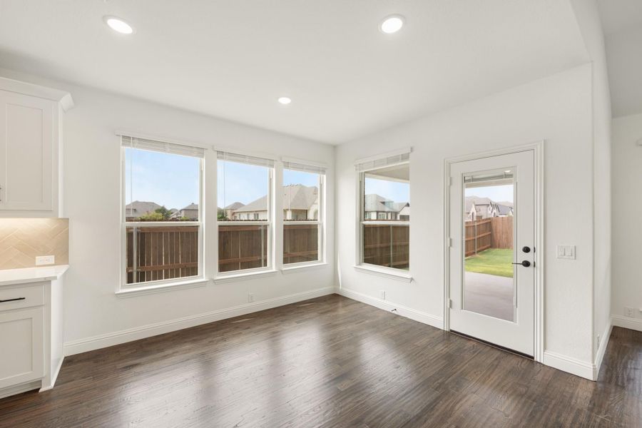 Bright dining area with dark hardwood floors, multiple windows, and a glass back door leading to the yard.