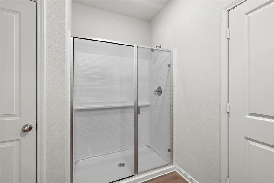 Full bath with a stall shower, a textured wall, and dark wood finished floors