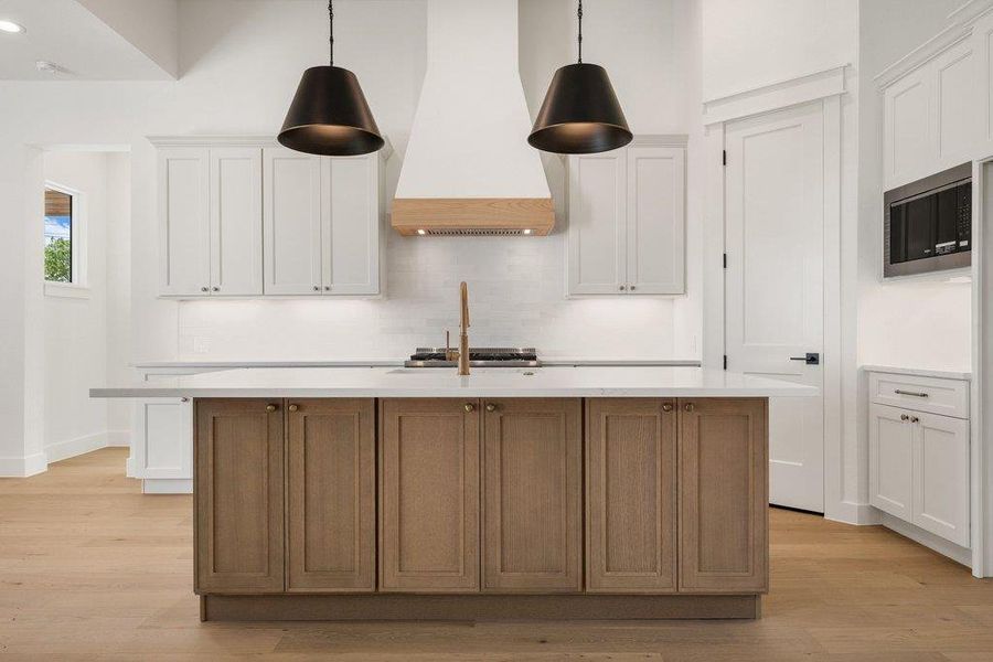 The kitchen features a large island with a light-colored countertop and wood cabinetry, complemented by white upper cabinets and a range hood with a wood accent