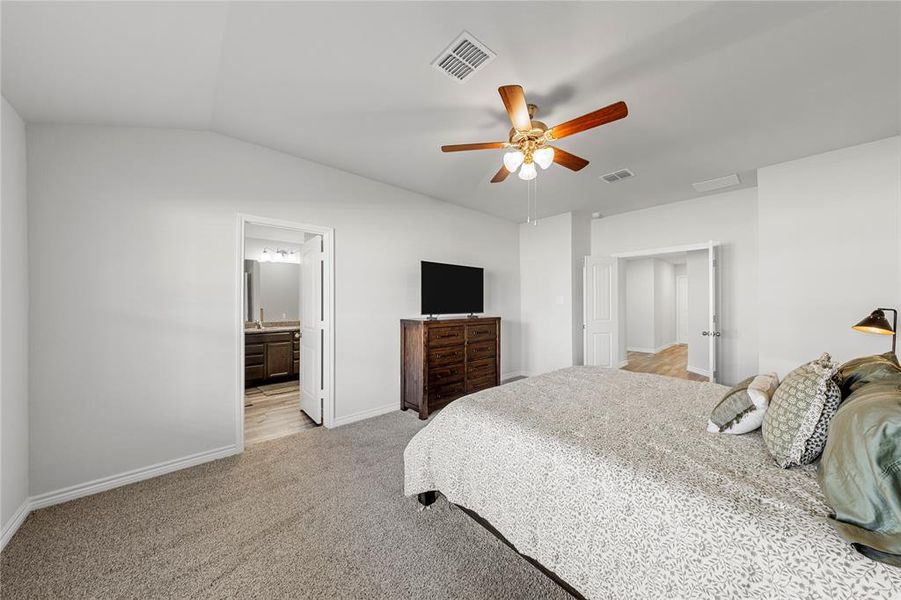 Bedroom with light colored carpet, vaulted ceiling, ceiling fan, and ensuite bath