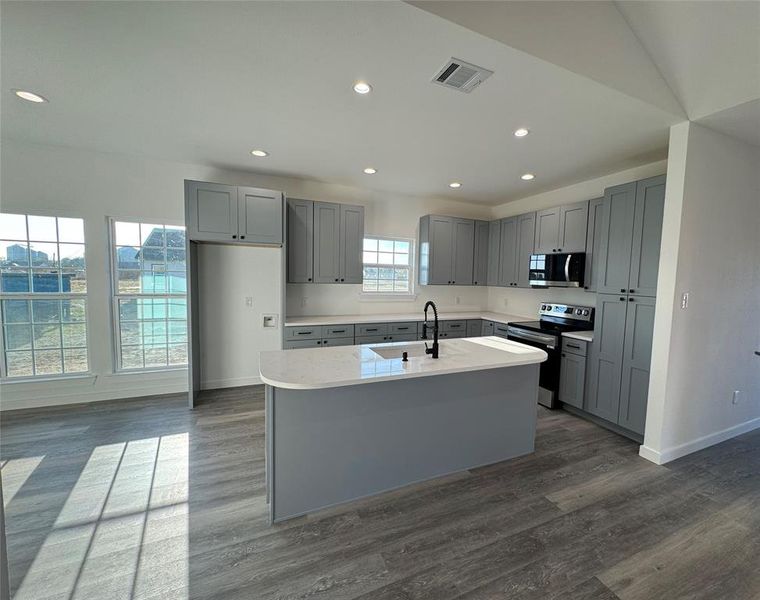 Kitchen with dark wood-type flooring, a center island with sink, sink, gray cabinets, and stainless steel appliances