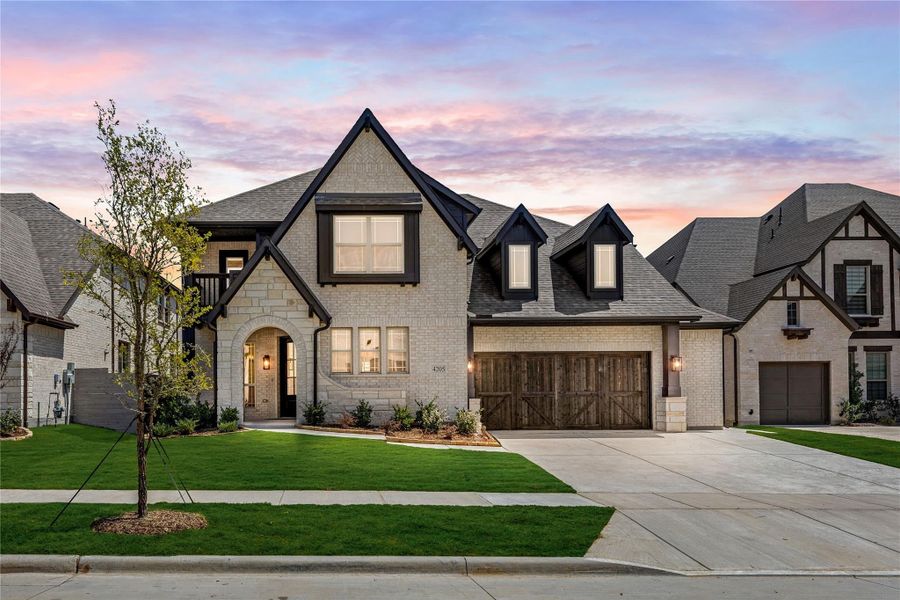 Two-story brick home with dark trim, arched entry, wood garage door, and manicured front lawn at dusk Two-story brick home with dark trim, arched entry, wood garage door, and manicured front lawn at dusk