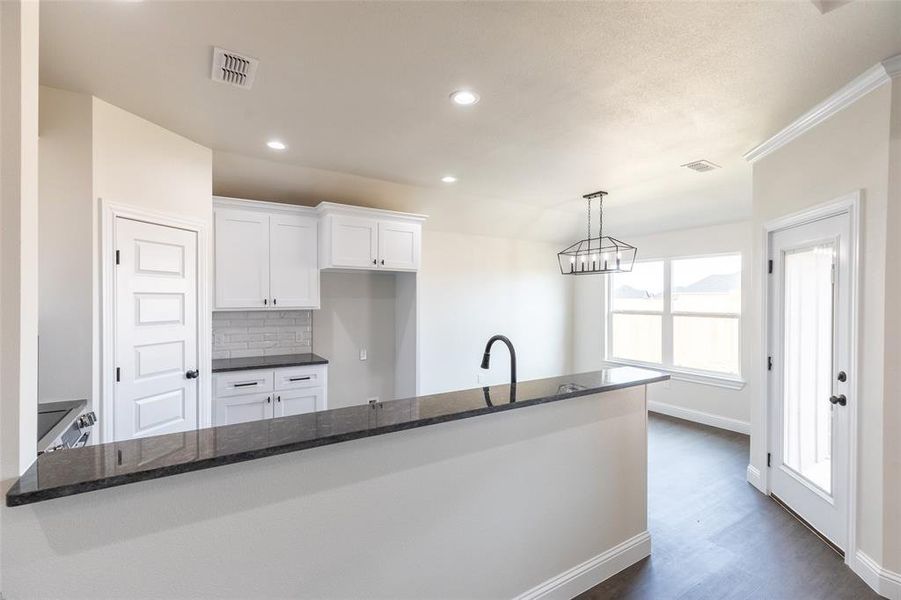 Kitchen featuring a breakfast bar with dark countertops, white cabinetry, subway tile backsplash, and a modern pendant light fixture