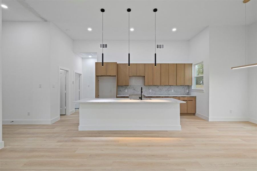 Kitchen featuring a high ceiling, pendant lighting, modern cabinets, a kitchen island with sink, and brown cabinetry