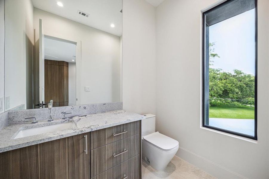 The game room powder room features Ibla Linfa natural floor tile, complemented by a Grohe widespread bathroom sink faucet in polished chrome and a Kohler undermount bathroom sink. It includes a Duravit one-piece toilet, recessed LED lighting, and designer neutral wall paint, offering both style and functionality in this convenient space.