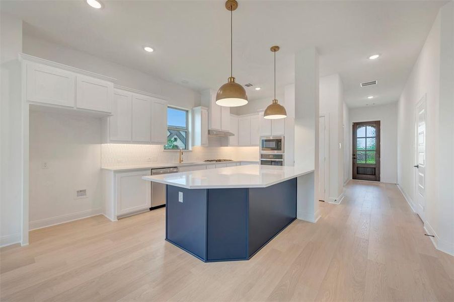 Kitchen featuring a blue island with a light-toned countertop, white cabinetry, integrated stainless steel appliances, and wood-finish flooring