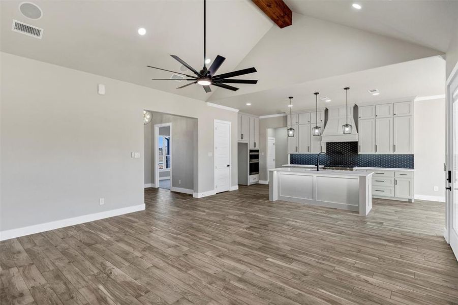 Kitchen featuring pendant lighting, white cabinets, a center island with sink, decorative backsplash, and beamed ceiling