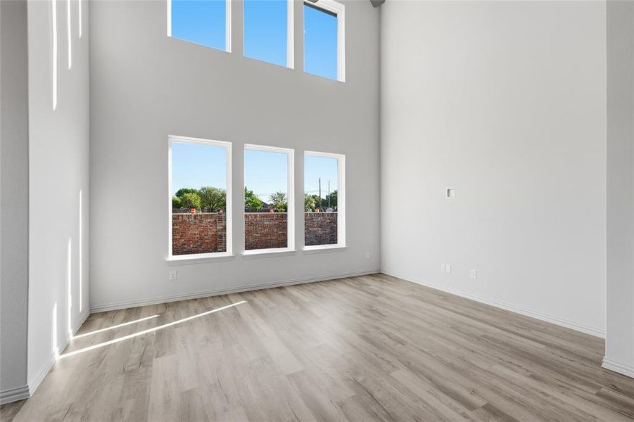 Unfurnished living room featuring light wood-type flooring and a high ceiling Unfurnished living room featuring light wood-type flooring and a high ceiling