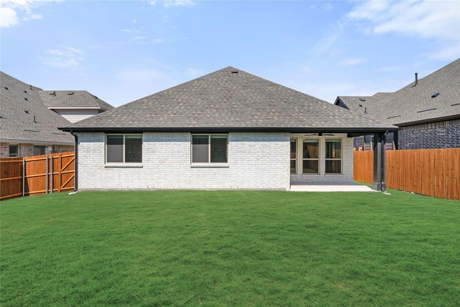 Rear view of single-story brick home with covered patio, large green lawn, and wood privacy fence. Rear view of single-story brick home with covered patio, large green lawn, and wood privacy fence.