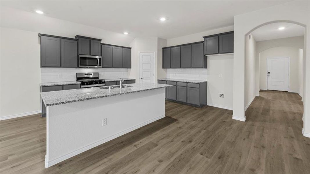Modern kitchen featuring gray cabinetry, stainless steel appliances, a white subway tile backsplash, and a spacious island with a light-colored speckled countertop