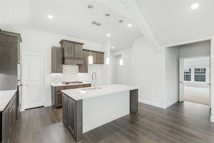 Kitchen with large white island, dark wood cabinets, pendant lights, and hardwood floors under vaulted ceiling Kitchen with large white island, dark wood cabinets, pendant lights, and hardwood floors under vaulted ceiling