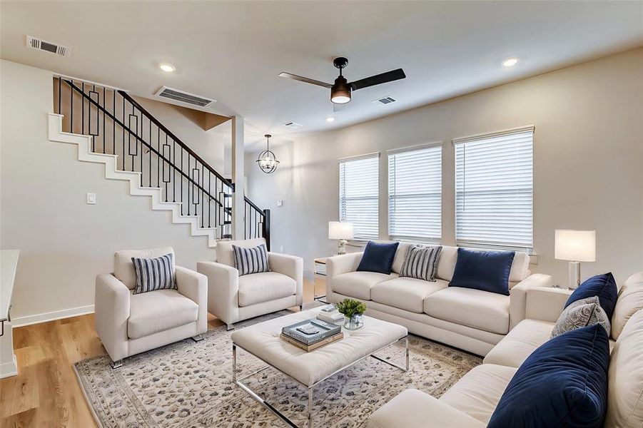 Natural light floods this spacious living area, featuring elegant wood flooring and a modern staircase with wrought iron accents. A harmonious blend of style and comfort awaits.