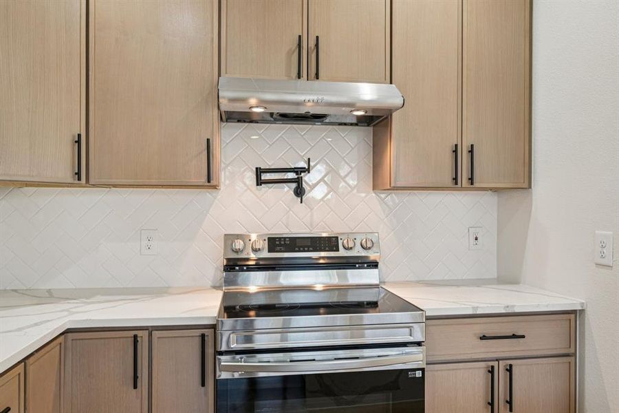 Kitchen with stainless steel electric range, light stone countertops, under cabinet range hood, and light brown cabinets