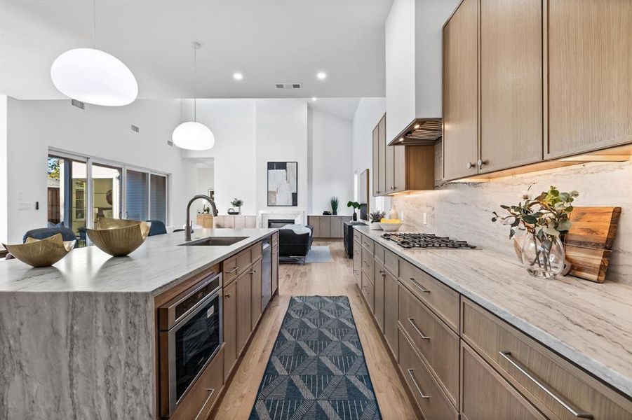 Kitchen with light stone countertops, hanging light fixtures, a spacious island, custom range hood, and light wood-type flooring