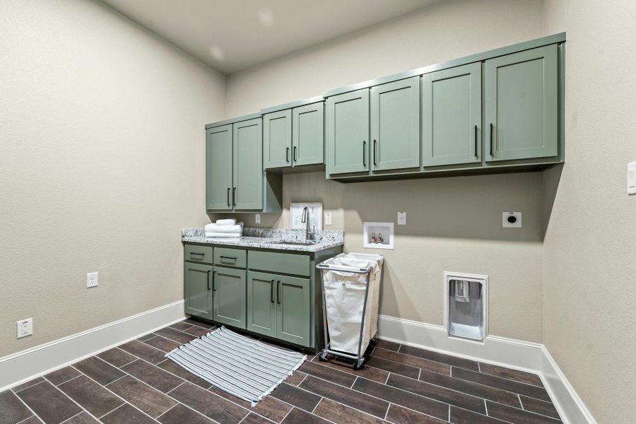 Utility room featuring dark wood-finish tile flooring, extensive sage green cabinetry with black hardware, a light-colored speckled countertop, and a stainless steel sink with a high-arc faucet