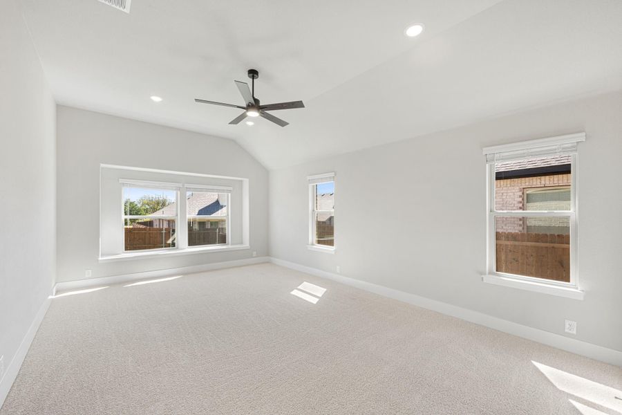 Empty bedroom with vaulted ceiling, ceiling fan, carpet flooring, and three windows