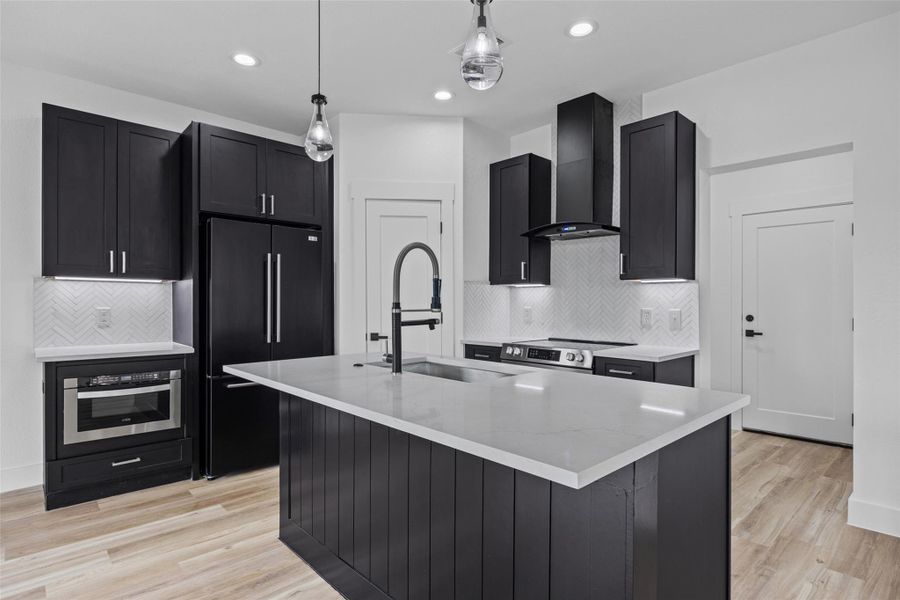 Contemporary kitchen featuring a large island with a matte black faucet, dark cabinetry, light countertops, and a white herringbone tile backsplash Contemporary kitchen featuring a large island with a matte black faucet, dark cabinetry, light countertops, and a white herringbone tile backsplash