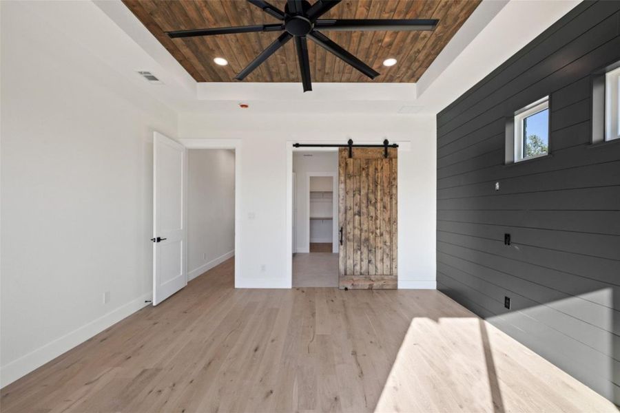A well-lit bedroom showcases light wood flooring and a distinctive shiplap accent wall, complemented by a rustic barn door. A well-lit bedroom showcases light wood flooring and a distinctive shiplap accent wall, complemented by a rustic barn door.