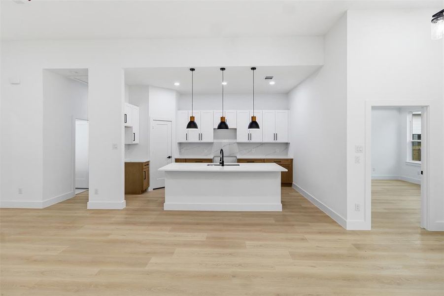 Kitchen with decorative light fixtures, an island with sink, white cabinetry, light wood-style floors, and open floor plan