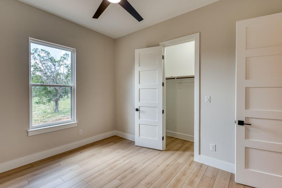 A quiet bedroom with light wood flooring features a window overlooking a verdant landscape.