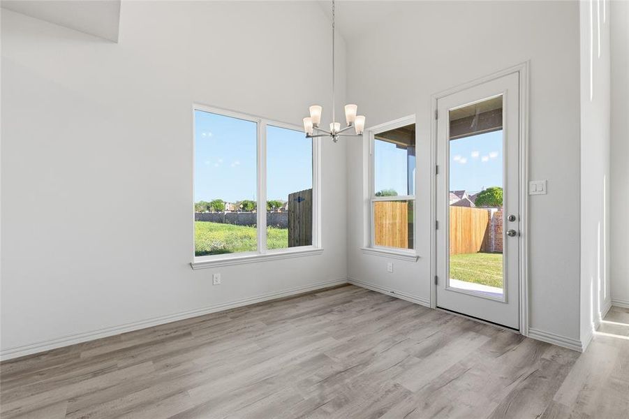 Unfurnished dining area featuring a chandelier, light wood-style flooring, and a high ceiling Unfurnished dining area featuring a chandelier, light wood-style flooring, and a high ceiling