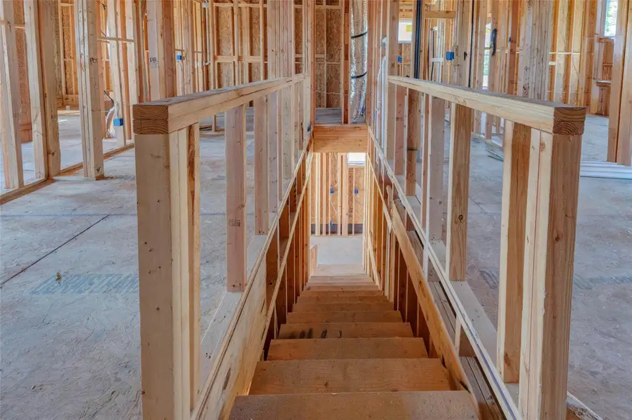 Upper-level staircase view looking down through the framed stair opening, showing exposed wood rail construction, surrounding room framing, and the connection between floors. This photo highlights the home’s two-story design, central circulation, and construction progress while giving buyers a clear sense of how the private upstairs spaces connect to the main level below. Upper-level staircase view looking down through the framed stair opening, showing exposed wood rail construction, surrounding room framing, and the connection between floors. This photo highlights the home’s two-story design, central circulation, and construction progress while giving buyers a clear sense of how the private upstairs spaces connect to the main level below.