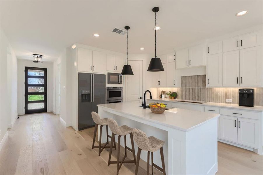 Virtually Staged Photo - Kitchen with light hardwood / wood-style flooring, backsplash, a center island with sink, white cabinetry, and black appliances