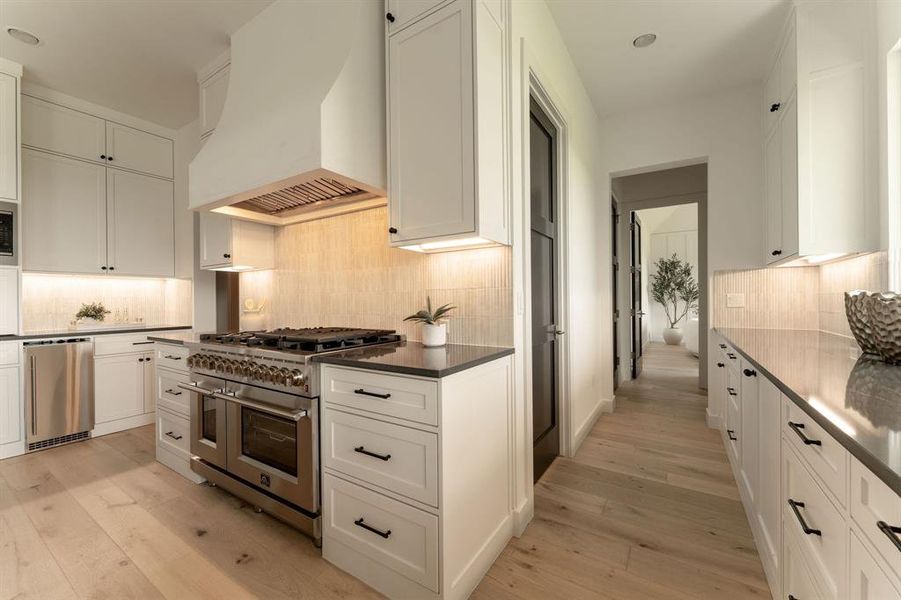 Kitchen with stainless steel appliances, custom exhaust hood, light wood-type flooring, white cabinetry, and recessed lighting Kitchen with stainless steel appliances, custom exhaust hood, light wood-type flooring, white cabinetry, and recessed lighting