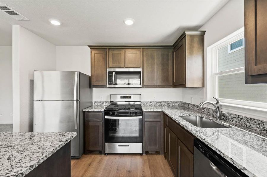 Kitchen with visible vents, appliances with stainless steel finishes, light stone counters, light wood-style floors, and a sink