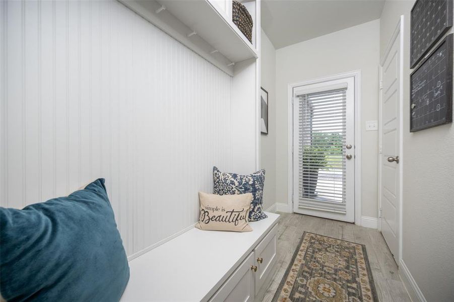 Built-in mudroom with bench seating, beadboard wall detail, overhead storage, and direct access to the back patio through the glass door.