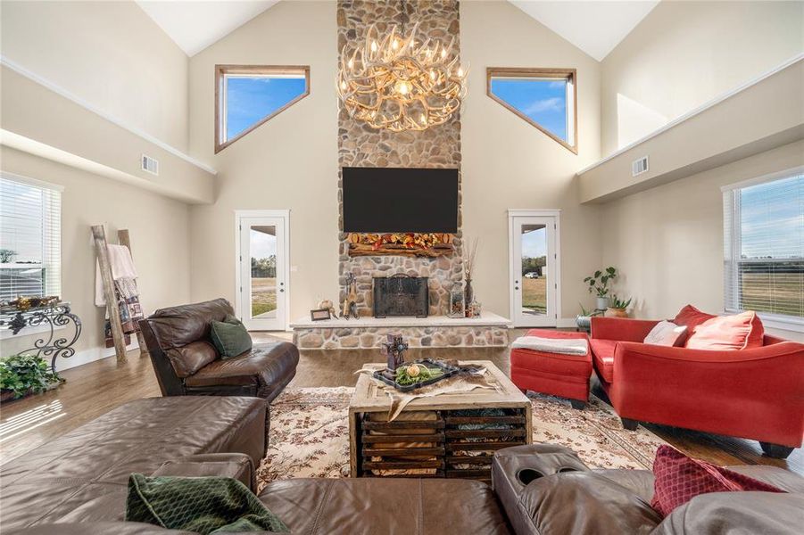 Living area with a chandelier, wood finished floors, a stone fireplace, plenty of natural light, and high vaulted ceiling