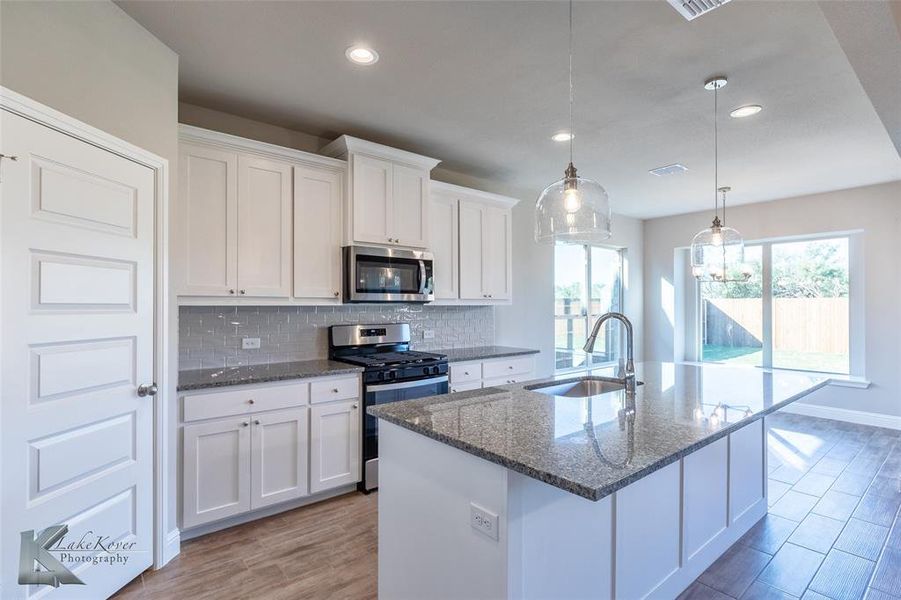 Kitchen featuring dark stone counters, appliances with stainless steel finishes, decorative backsplash, white cabinetry, and light wood-style floors