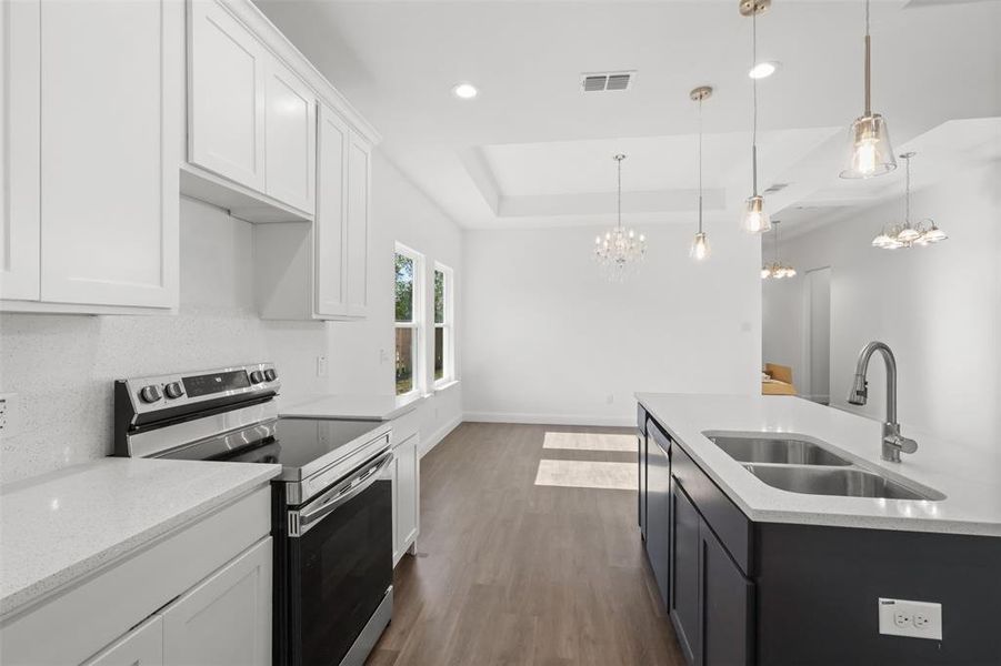 Kitchen with electric stove, sink, white cabinets, and hanging light fixtures