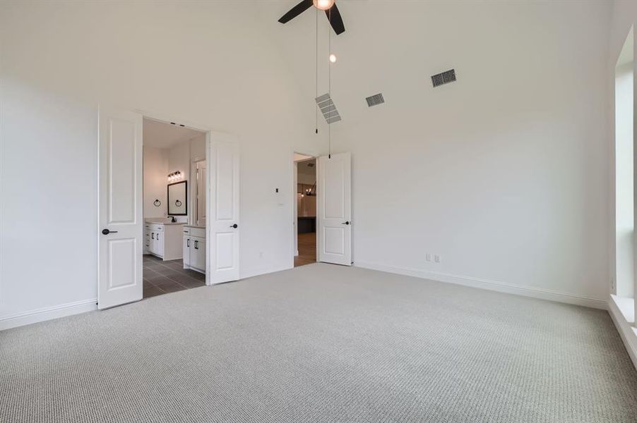 Unfurnished bedroom with connected bathroom, ceiling fan, high vaulted ceiling, and dark colored carpet