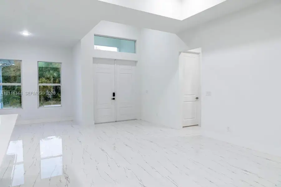 Double-door entry featuring a transom window, high ceilings, large-format tile flooring with veining detail, and tall, multi-pane windows Double-door entry featuring a transom window, high ceilings, large-format tile flooring with veining detail, and tall, multi-pane windows