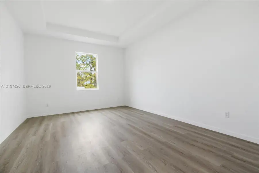 Interior room featuring a tray ceiling, neutral wall tones, and wood-finish flooring Interior room featuring a tray ceiling, neutral wall tones, and wood-finish flooring
